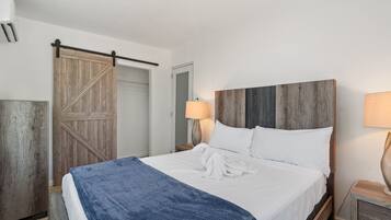 Una cama bien tendida con una manta azul, cabecera de madera y una puerta corredera de madera.