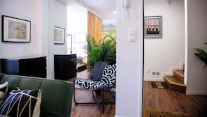 A modern living room with a green sofa, a black and white patterned chair, and a wooden staircase leading to another room.