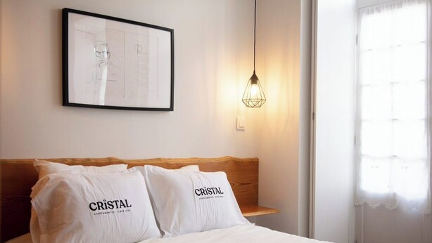 A neatly made bed with two pillows labeled "CRISTAL" and a framed sketch on the wall.
