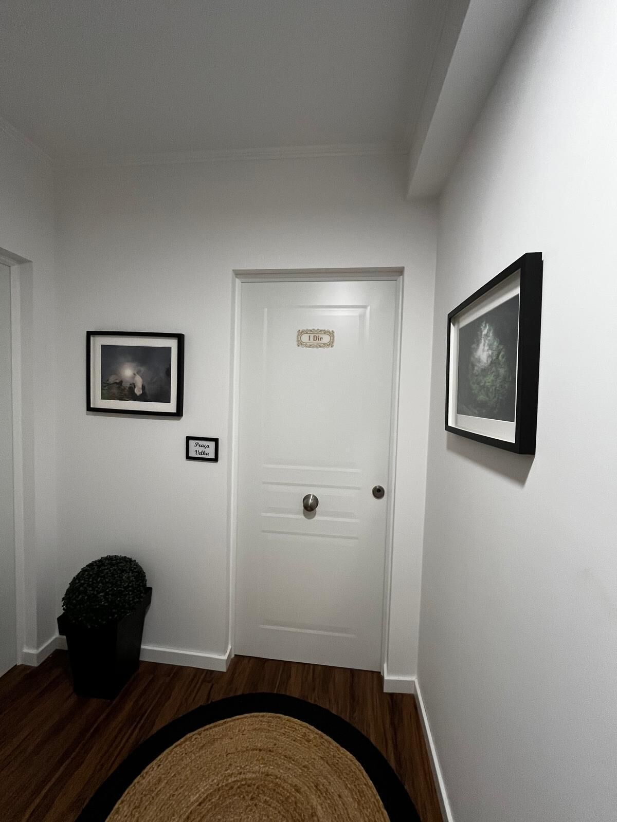 A hallway with a white door, a framed picture on the left, and another on the right.