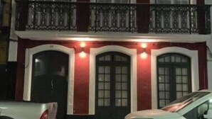 A two-story building with a red facade, multiple windows, and a balcony with black railings.