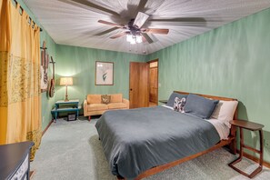 Ein Schlafzimmer mit einem Bett, einem Deckenventilator, einem Nachttisch, einer Lampe, einem Sessel und einer Tür.