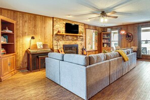 Ein Wohnzimmer mit Ecksofa, Kamin, Fernseher an einer Ziegelwand und Deckenventilator.