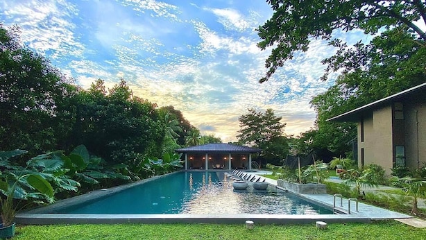 Una piscina con un pabellón, rodeada de abundante vegetación y un cielo despejado.