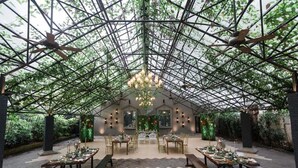 Un jardín interior con techo de vidrio, mesas dispuestas para comer y una lámpara central.