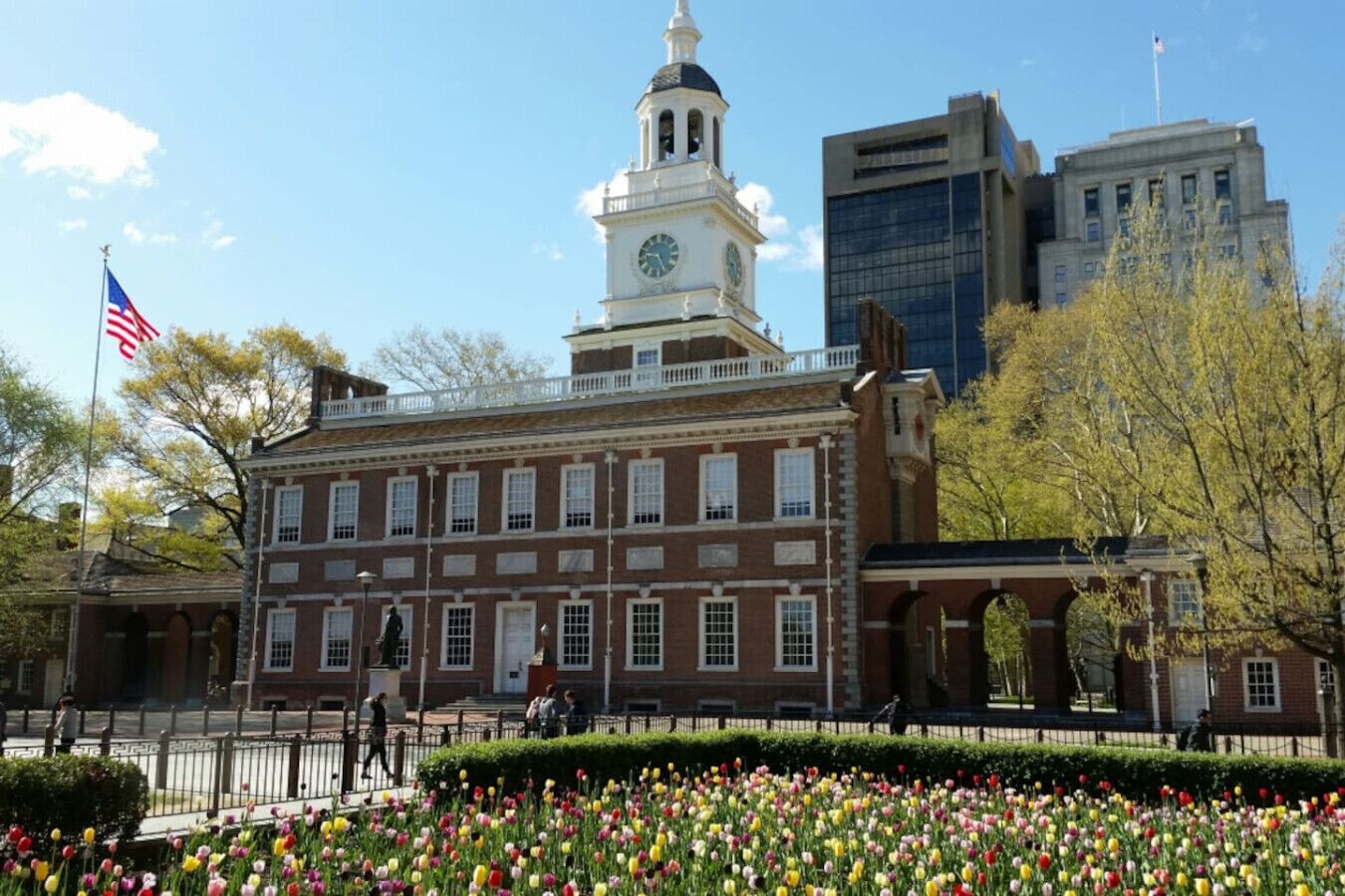 A historic building with a clock tower, surrounded by a garden of tulips and a flag.