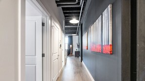 Un pasillo con puertas blancas, suelo de madera y una pared oscura con obra de arte roja.