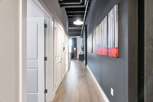 Un pasillo con puertas blancas, suelo de madera y una pared oscura con obra de arte roja.