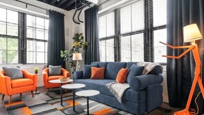 Una sala de estar moderna con un sofá azul, sillones naranjas y una lámpara de pie naranja original.