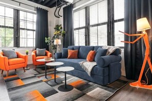 A modern living room with a blue sofa, orange armchairs, and a unique orange floor lamp.