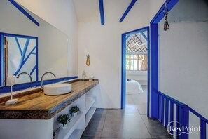 A bathroom with a wooden vanity, a white sink, and a mirror. There is a towel rack and a hanging towel. The walls are painted white with blue trim. - New KeyPöint: Tröpical House with incredible view! (Palomino)