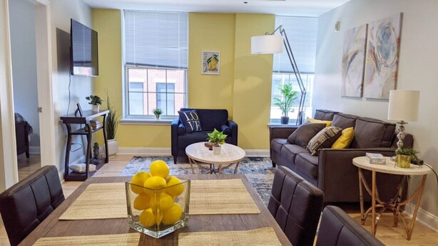 A modern living room with a sofa, armchairs, a coffee table, and a dining area with a glass vase of lemons.