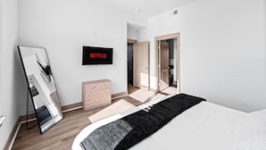 A modern bedroom with a bed, a TV mounted on the wall, a mirror, and a wooden dresser.