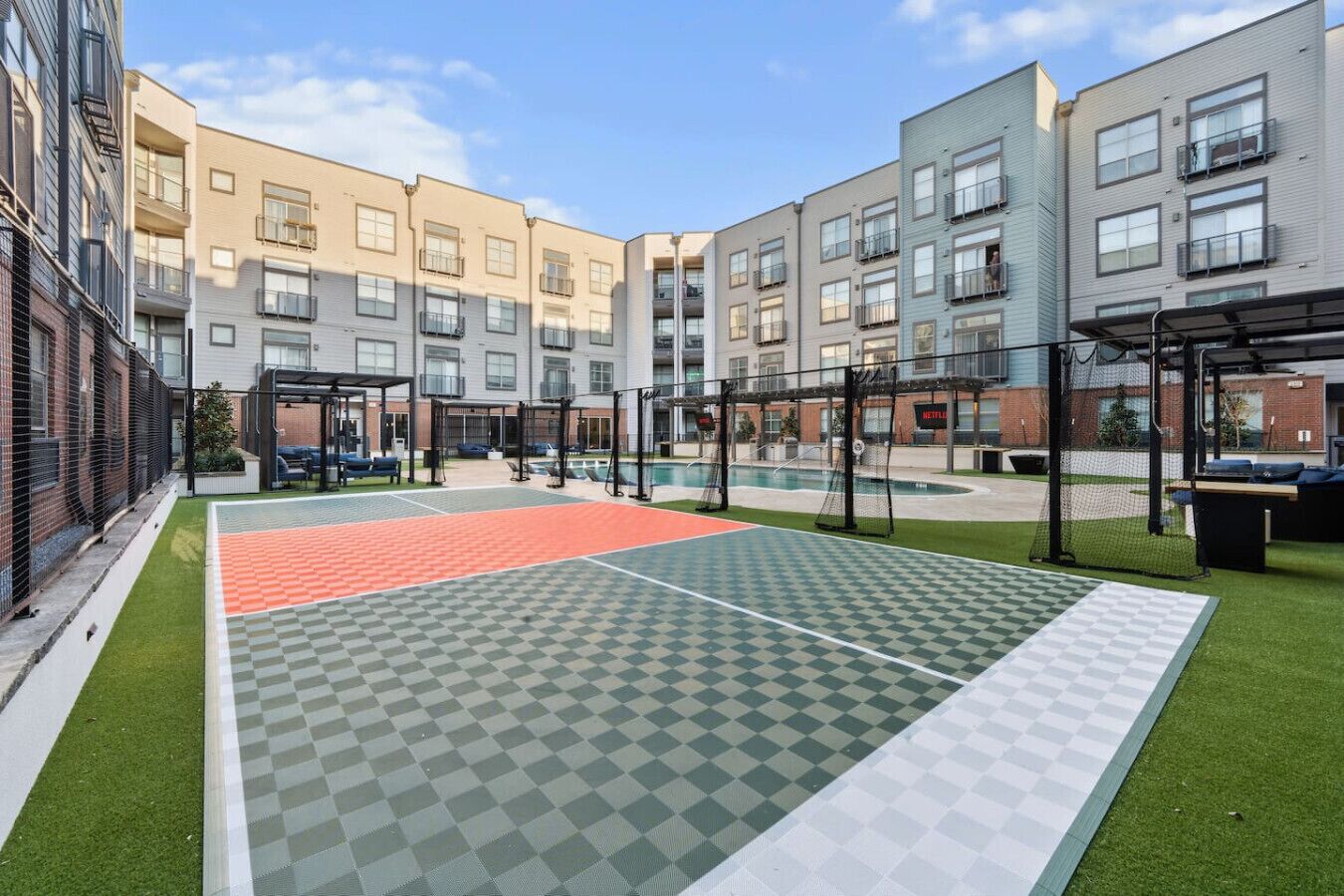 Une cour avec un espace extérieur carrelé, une piscine et des immeubles d’habitation en arrière-plan.
