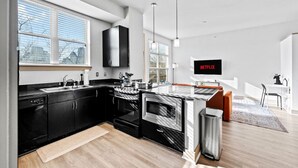 A modern kitchen with black cabinets, a microwave, and a sink. There is a dining area with a TV displaying 'NETFLIX' and a small table.