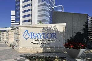 A sign for Baylor Charles A. Sammons Cancer Center with a modern building in the background. - 1Br Apt in Deep Ellum with King bed, Pool & Outdoor Space (Dallas)