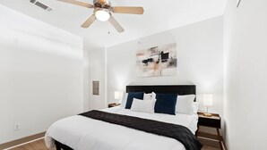 Un dormitorio moderno con una cama grande, un ventilador de techo y un cuadro en la pared.