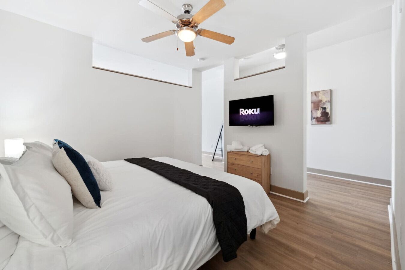 A modern bedroom with a bed, a ceiling fan, a TV, and a wooden dresser.