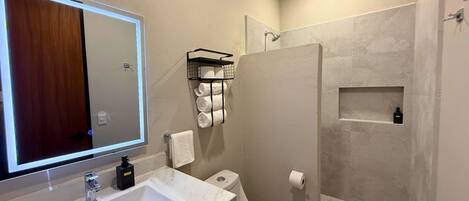 A modern bathroom with a large mirror, a sink, a toilet, and a shower area.