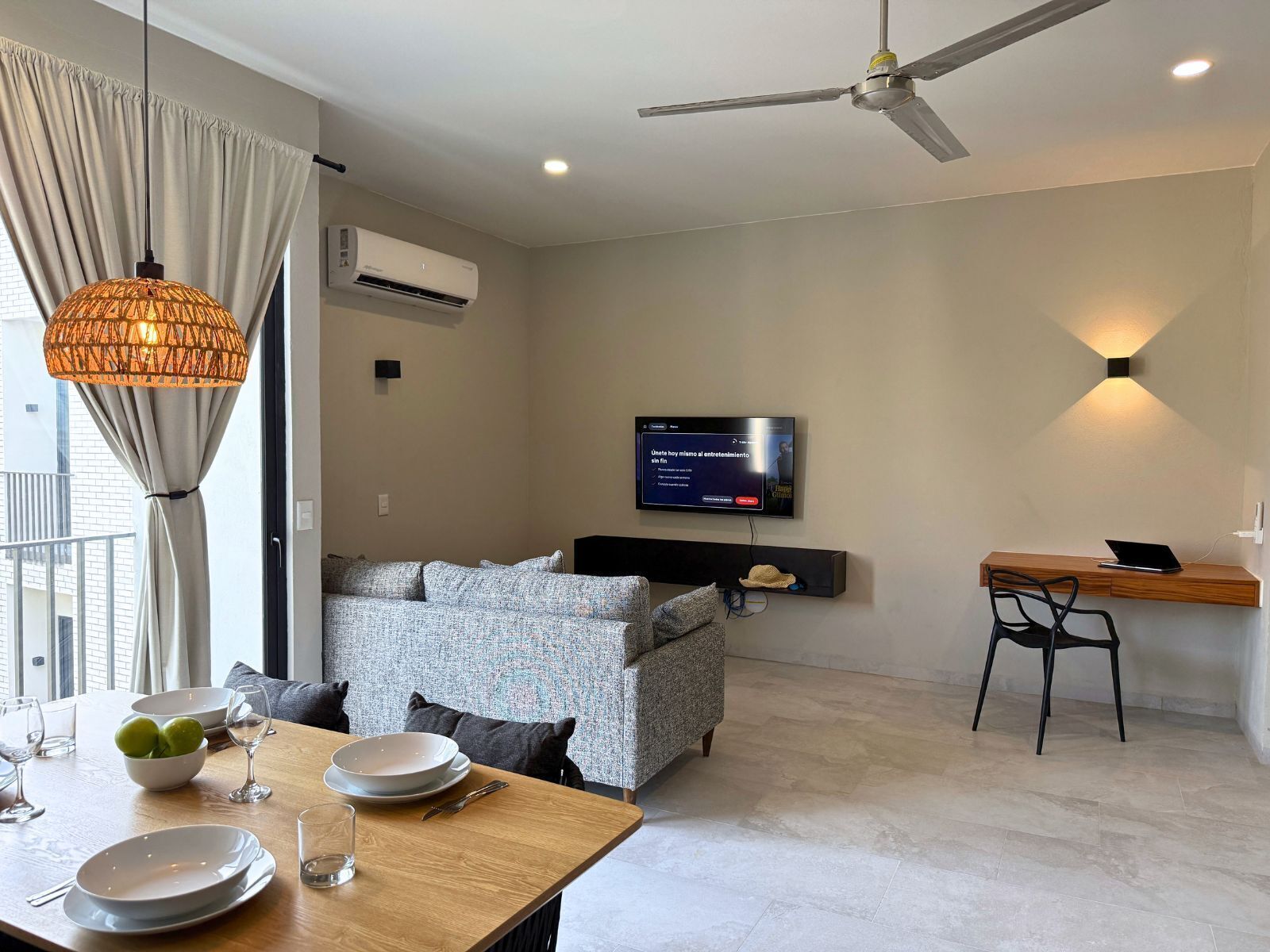 Una sala de estar moderna con un sofá, una mesa de comedor y un televisor montado en la pared.