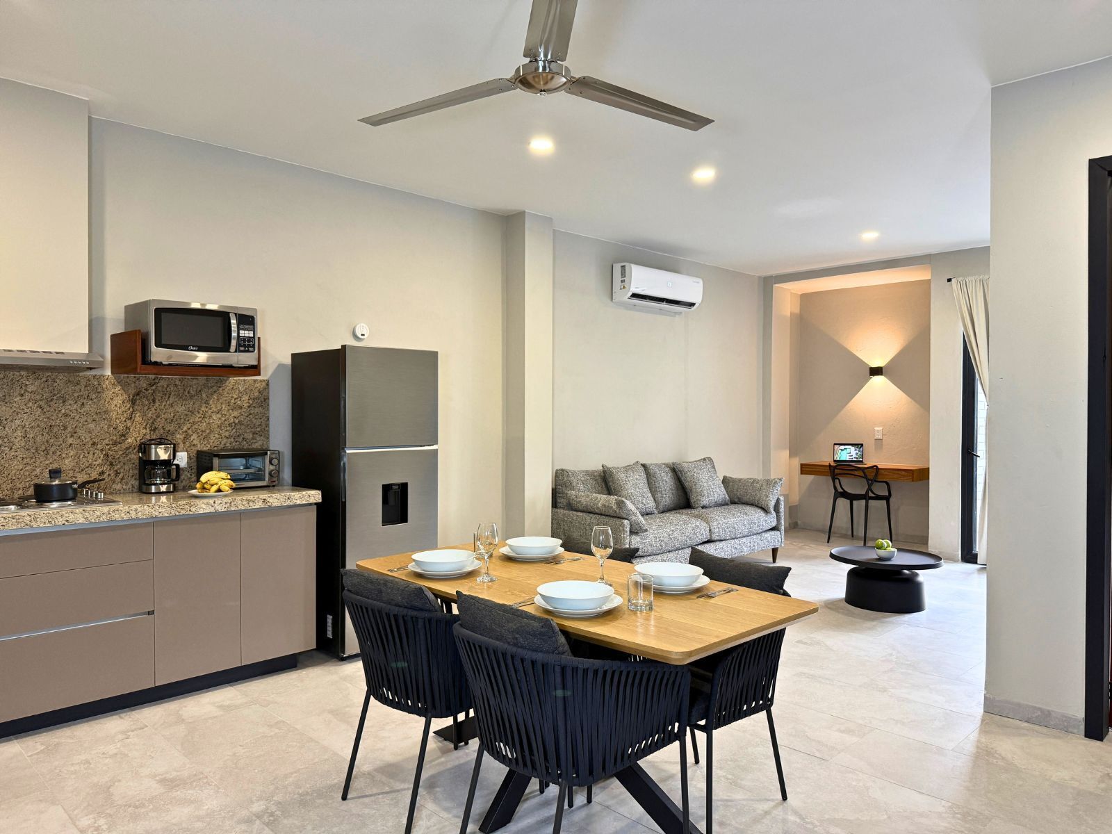A modern kitchen with a dining area, including a table set for four, a sofa, and a TV.