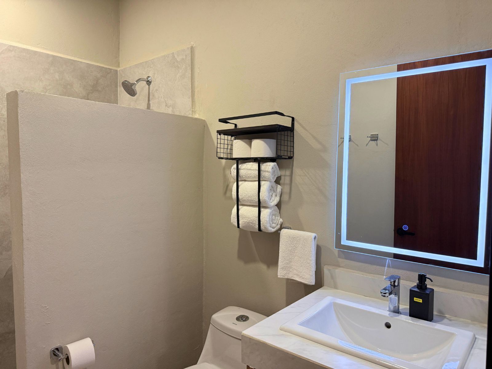 A bathroom with a toilet, sink, mirror, towel rack, and shower.