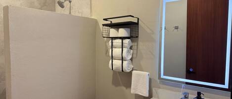 A bathroom with a toilet, sink, mirror, towel rack, and shower.