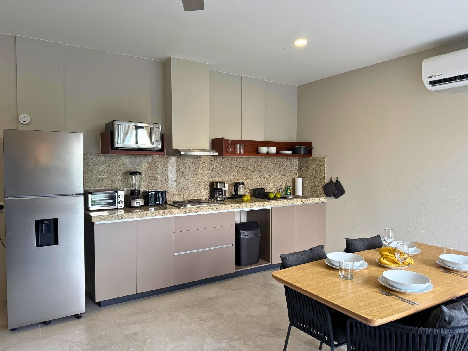 Cozinha moderna com micro-ondas, torradeira e cafeteira embutidos. Possui um espaço de jantar com mesa e cadeiras.