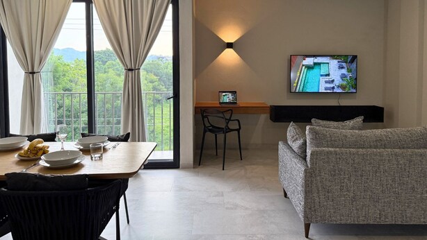 A modern room with a dining table set for two, a sofa, a desk with a laptop, and a TV displaying a pool view. - Rooms M (Santa María Huatulco)