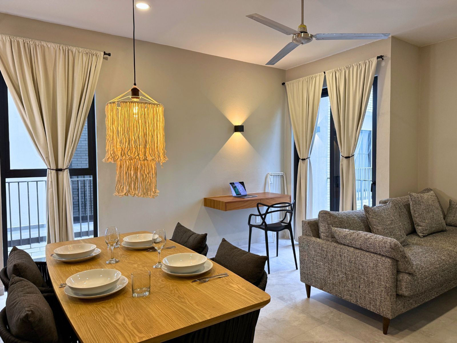 A modern living room with a dining area, a ceiling fan, and a laptop on a wooden shelf.