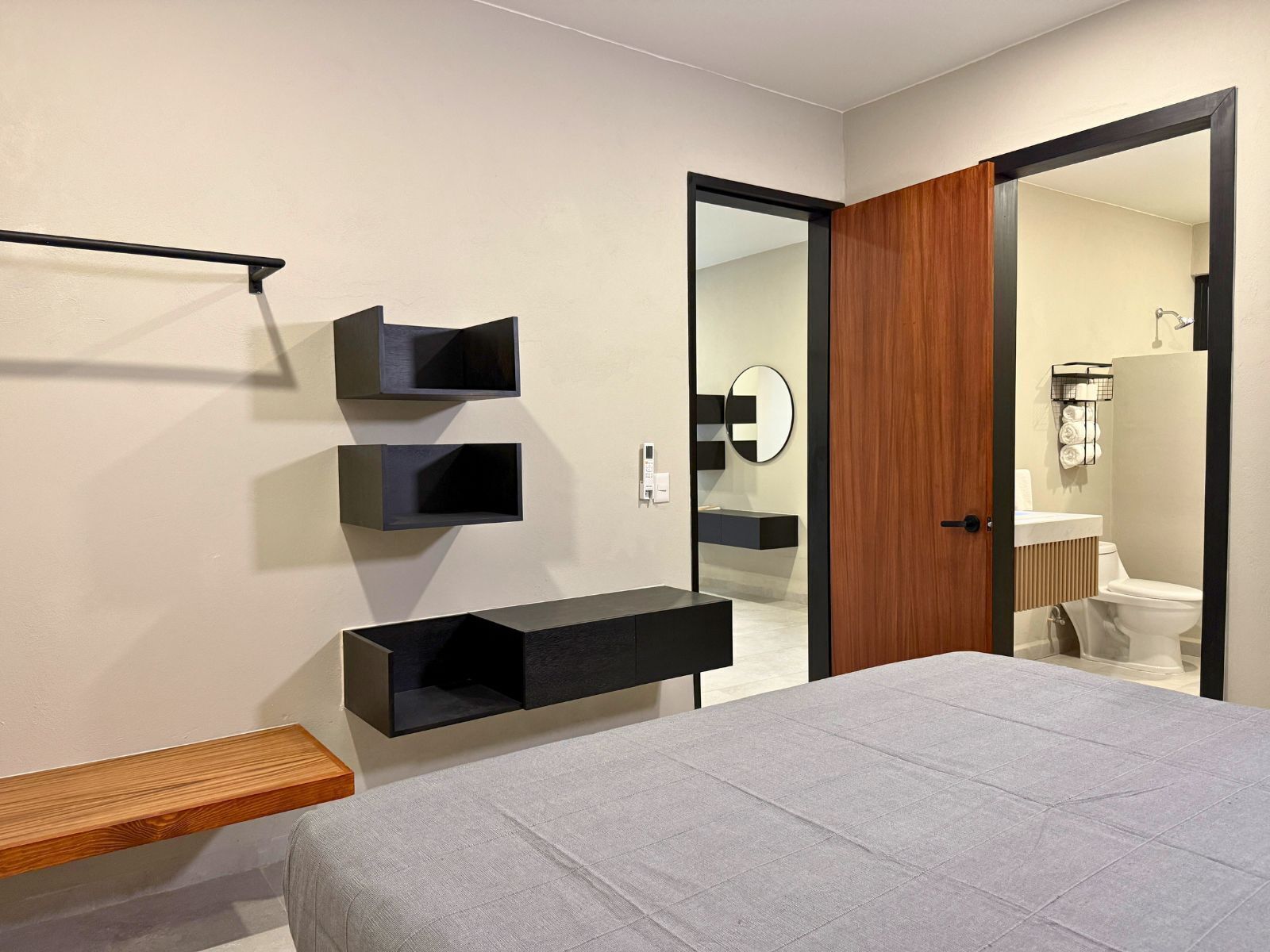 Un dormitorio moderno con una cama, un banco de madera y estanterías negras empotradas.