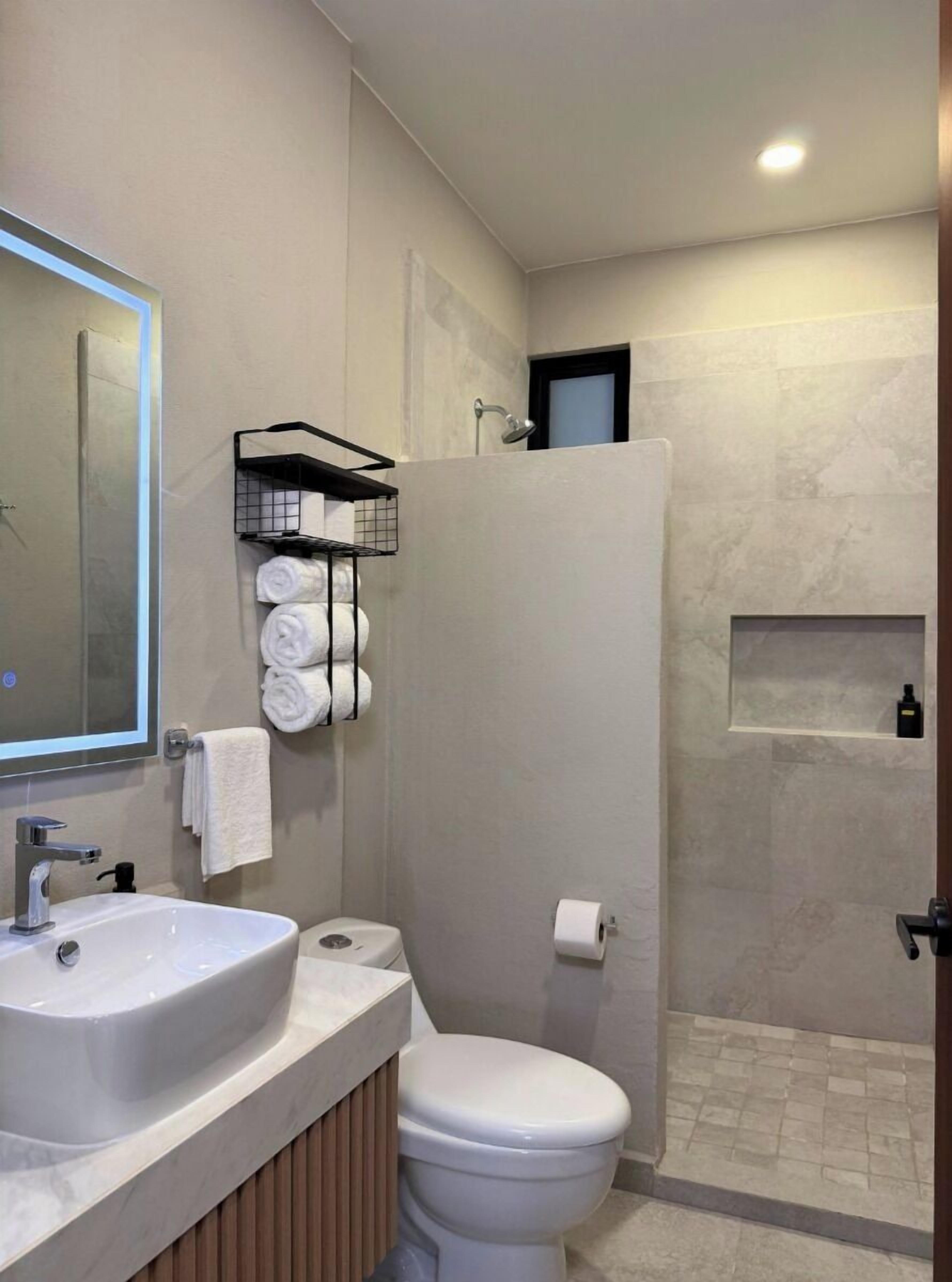 A modern bathroom with a large mirror, a sink, a toilet, and a shower area.