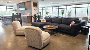 A modern lounge area with a sofa, two armchairs, a coffee table, and a small bar area with a sign.