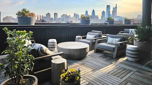 A rooftop terrace with outdoor seating, potted plants, and a city skyline view.