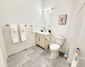 Une salle de bain moderne avec des toilettes, un lavabo et un miroir. Des serviettes sont suspendues sur un porte-serviettes et un tableau est accroché au mur.