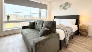 A bedroom with a large window, a sofa, a bed, and a nightstand.