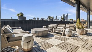 A rooftop terrace with outdoor seating, potted plants, and a city skyline view.