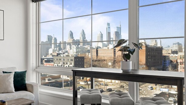 A room with a large window, a sofa, a table, and a potted plant.