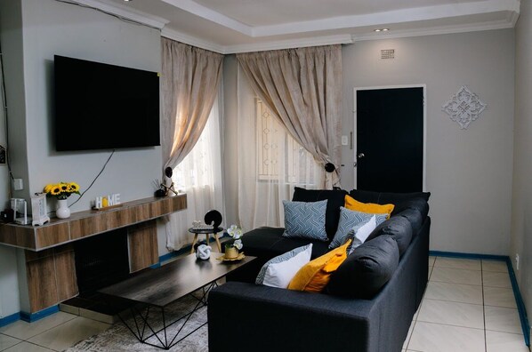 A modern living room with a black sofa, a coffee table, a flat-screen TV mounted on the wall, and a wooden console table with a vase of flowers.