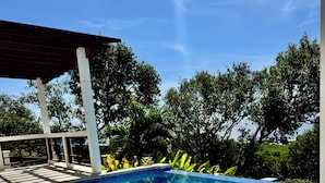 En swimmingpool med ett kaklat poolområde, en överbyggd sittplats och ett bord med en drink och limeskivor.