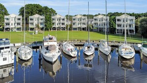 A marina with multiple boats docked, surrounded by multi-story buildings with balconies. - The Captain’s Quarters (New Bern)