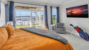 A bedroom with an orange bedspread, a view of a marina, a ceiling fan, and a golf bag. - The Captain’s Quarters (New Bern)
