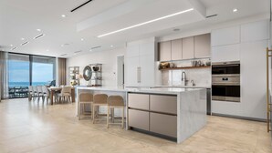 A modern kitchen with a large island, built-in appliances, and a dining area with a view. - Aqualina 1001 in Nassau (Nassau)