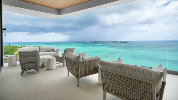 A balcony with wicker furniture, a white sofa, and a view of the ocean. - Aqualina 1001 in Nassau (Nassau)