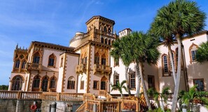 A historic building with ornate architecture, including arched windows and balconies, surrounded by palm trees.