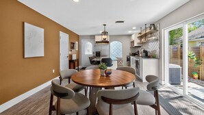 Una cocina moderna con una isla central, un comedor con una mesa redonda y sillas, y un amplio ventanal corredero que da a un patio trasero.