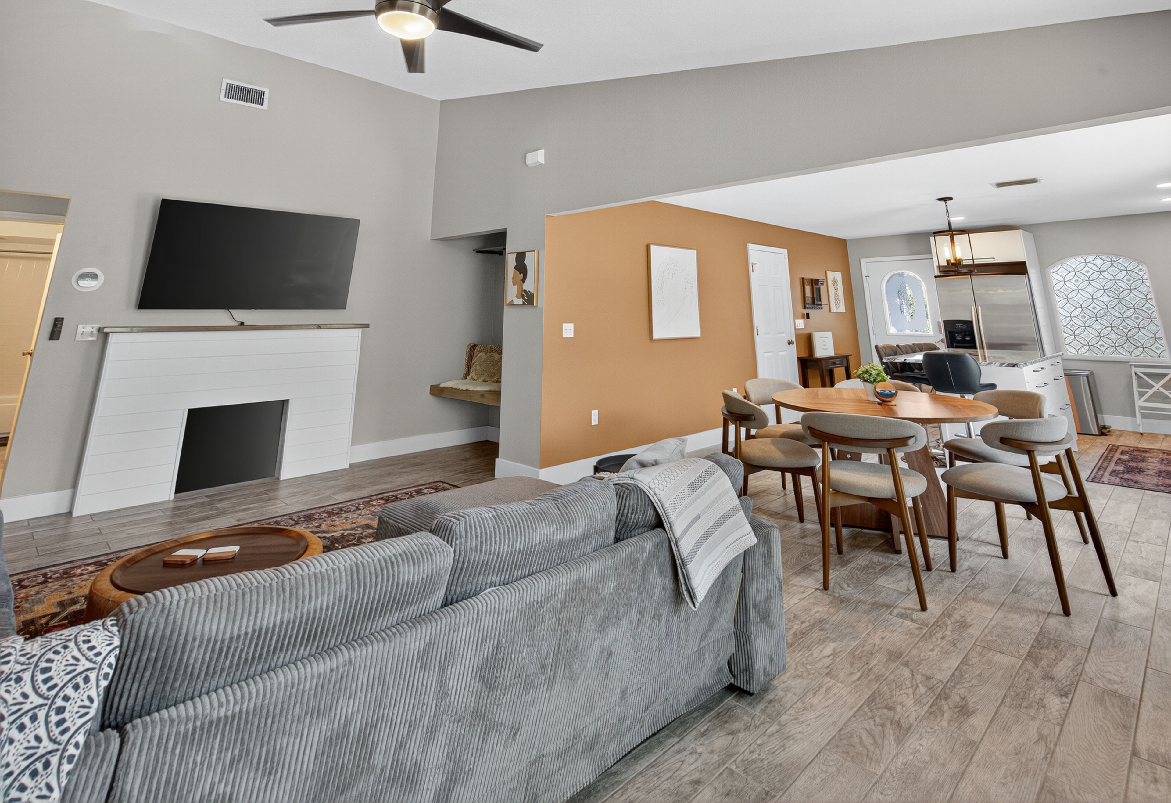A modern living room with a gray sofa, dining table, and chairs, a flat-screen TV, and a fireplace.