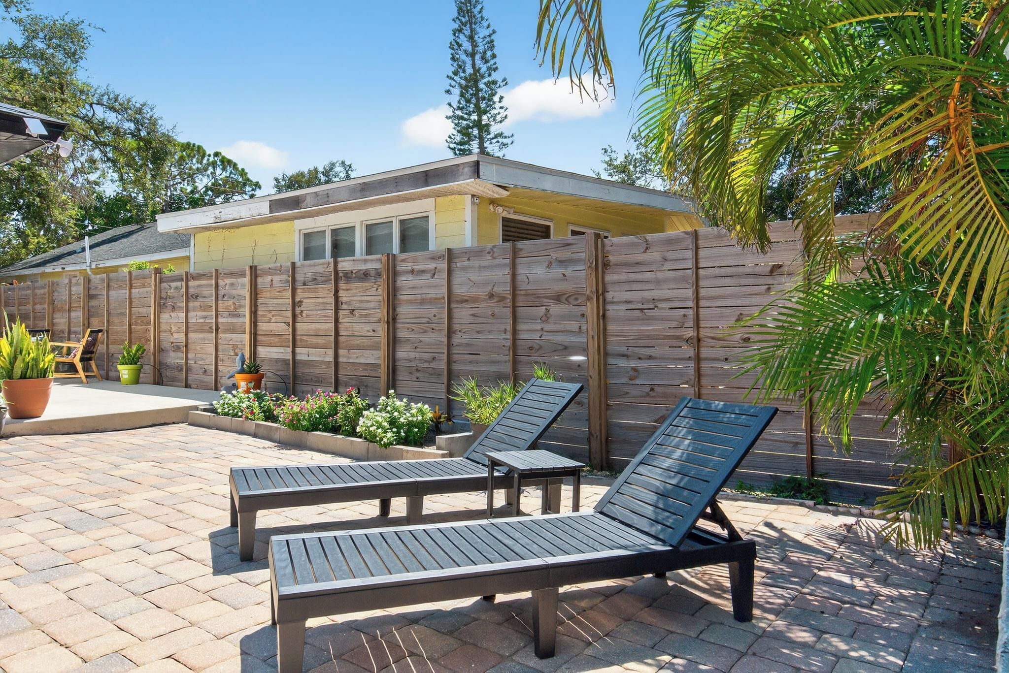 Un espace patio aménagé avec deux chaises longues, une clôture en bois et des plantes en pot.
