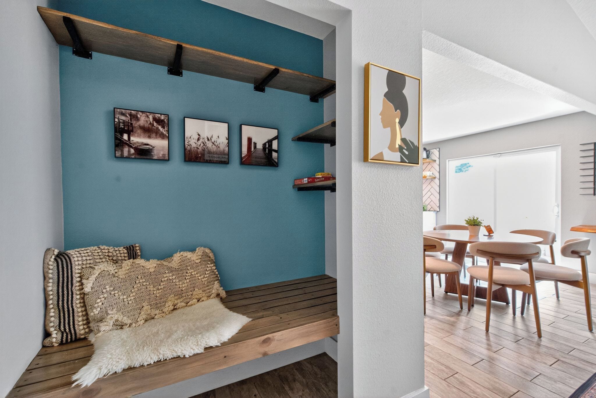 A cozy seating area with a bench, a wall-mounted shelf with books, and framed pictures.