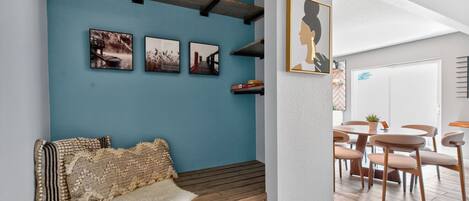A cozy seating area with a bench, a wall-mounted shelf with books, and framed pictures.